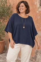 Pull ample marine à manches chauve-souris porté avec un sautoir cœur doré et un pantalon écru.