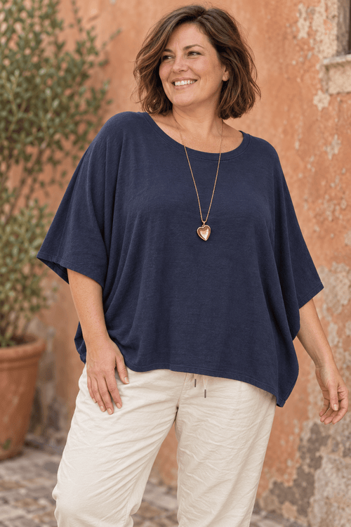 Pull ample marine à manches chauve-souris porté avec un sautoir cœur doré et un pantalon écru.