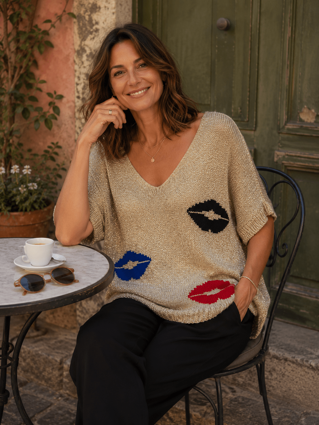 Pull Bella champagne doré à motifs bouches porté avec pantalon noir sur une terrasse italienne