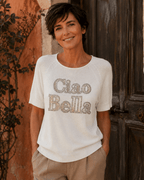 Femme portant le pull Ciao Bella blanc en coton avec message en strass et pantalon beige dans une ambiance italienne