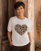 Femme portant le pull Cuore blanc à cœur léopard et strass avec pantalon chocolat devant une porte ancienne en Italie
