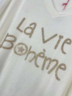 Détail inscription dorée pailletée “La Vie Bohème” sur pull col V femme