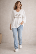 Pull blanc femme col V “La Vie Bohème” doré, coupe fluide, porté avec jean clair et sneakers blanches