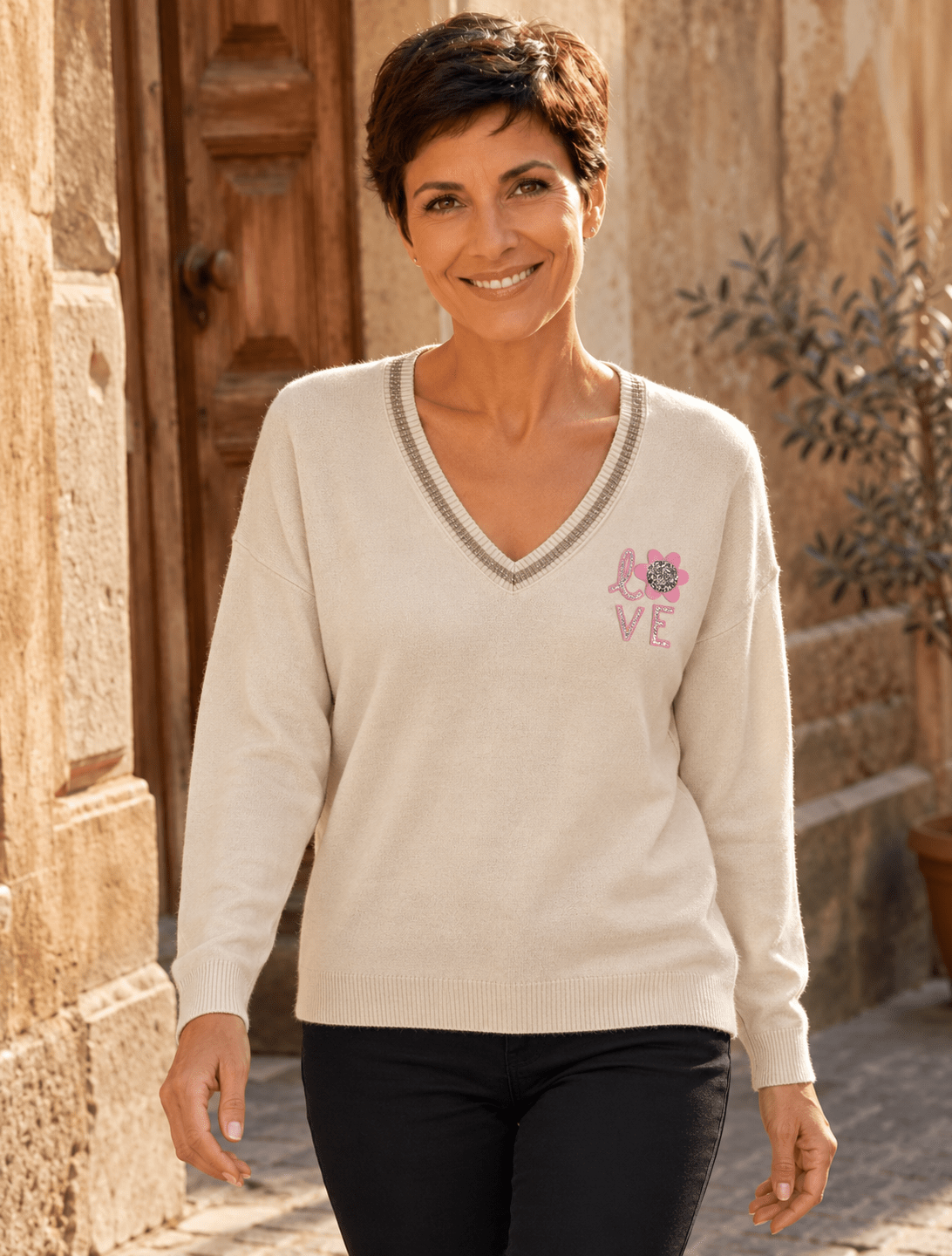 Sofia portant le pull Lucia beige à manches longues, avec le bas du pull laissé libre sur un pantalon noir.