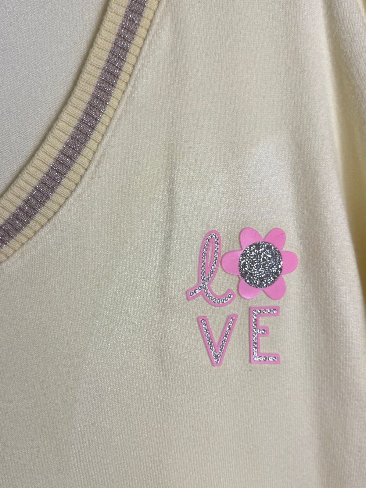Gros plan du motif LOVE rose, de la fleur et des strass du pull Lucia.