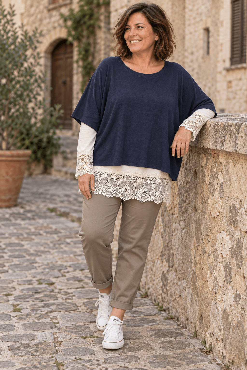 Pull marine porté sur un rouleau écru dont la dentelle dépasse aux manches et sous le bas, avec un pantalon taupe.