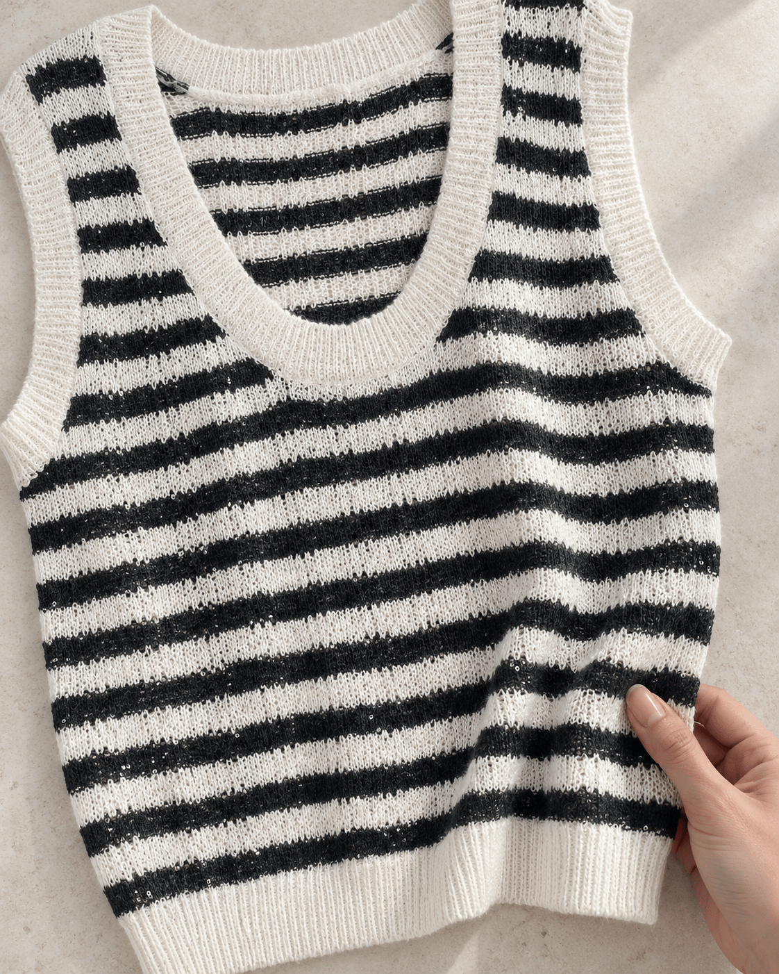 Détail de la maille rayée noire et écrue du pull Solène, avec une main posée sur le tissu