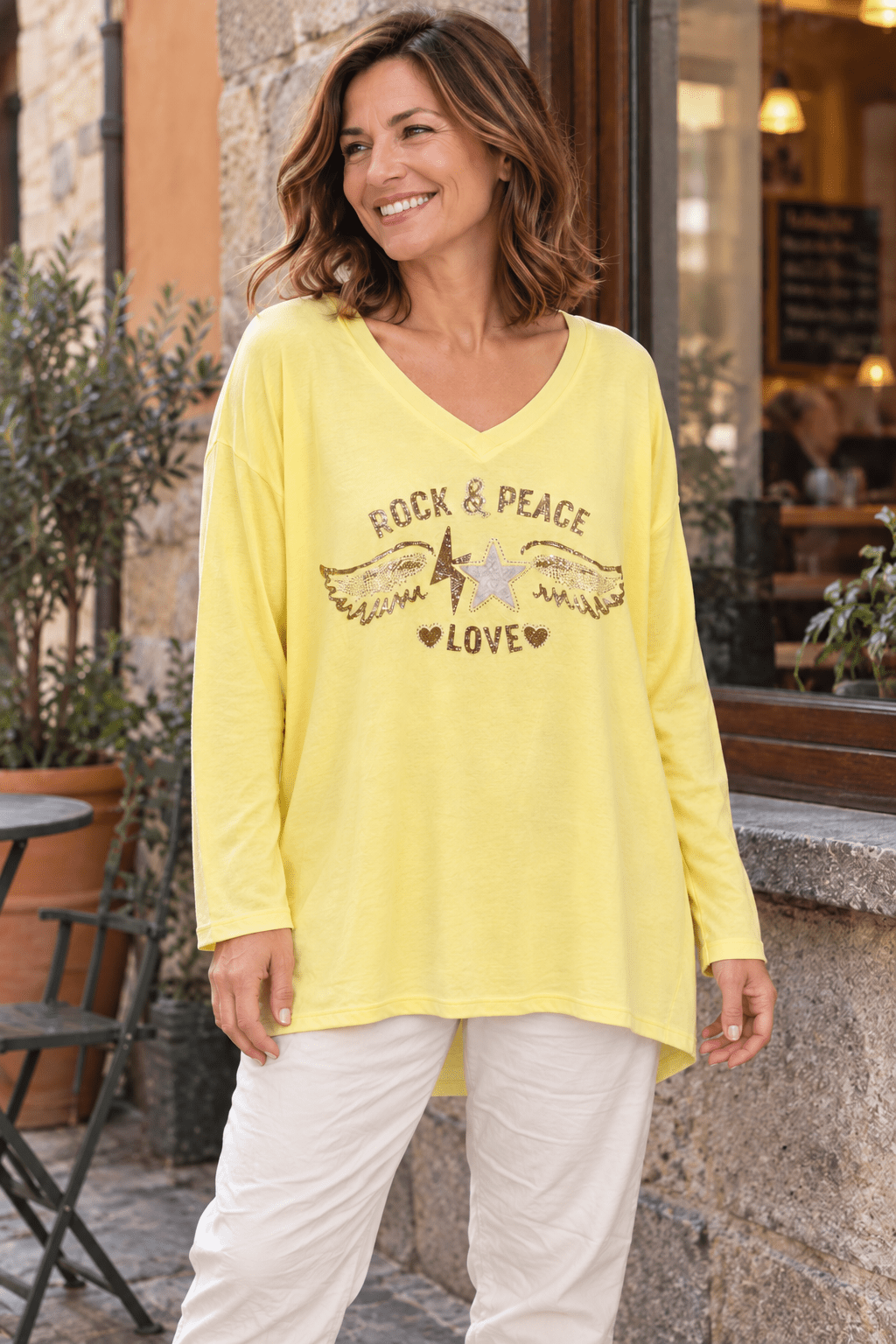 Pull Stella jaune pâle porté avec un pantalon écru, motif ailes, étoile et strass visible de face. (Mise en scène IA.)
