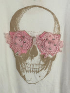 Détail des deux fleurs roses et des strass sur le pull blanc à tête de mort.