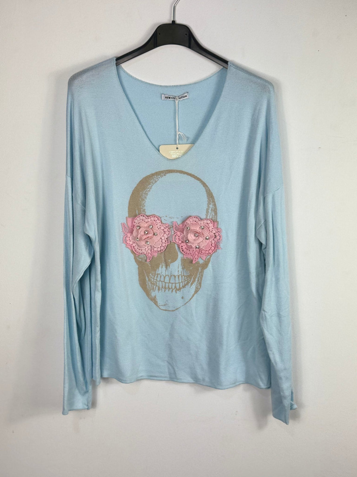 Pull bleu ciel sur cintre, col V et tête de mort à fleurs roses.