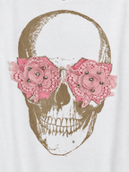 Photo retouchée en gros plan des fleurs roses à strass sur la tête de mort dorée du pull blanc.