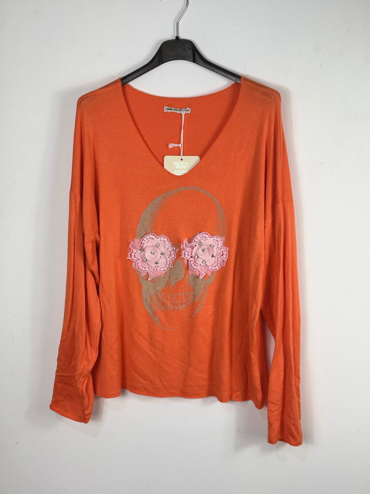Pull orange sur cintre avec tête de mort dorée et fleurs roses en relief.