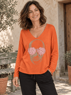 Pull orange à tête de mort fleurie porté avec un pantalon noir, bas du pull laissé libre.