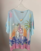 Pull femme bleu ciel en maille pailletée avec grand toucan tropical coloré sur le devant, vue de face