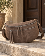 Sac banane chocolat effet serpent en simili-daim posé sur une marche en pierre, avec zips argentés et bandoulière assortie.