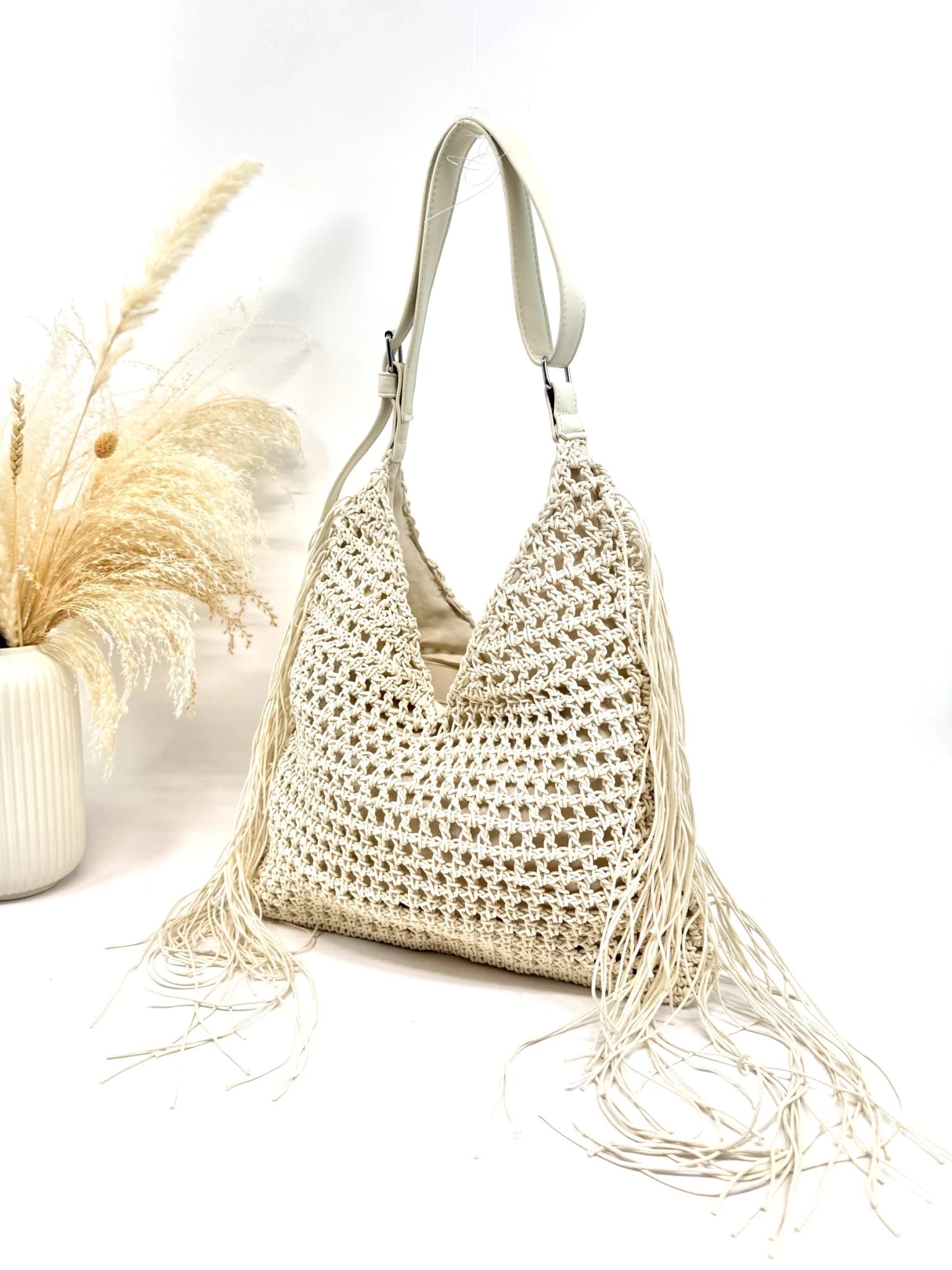 Sac hobo macramé beige avec franges latérales posé sur une table vue profil  femme bohème