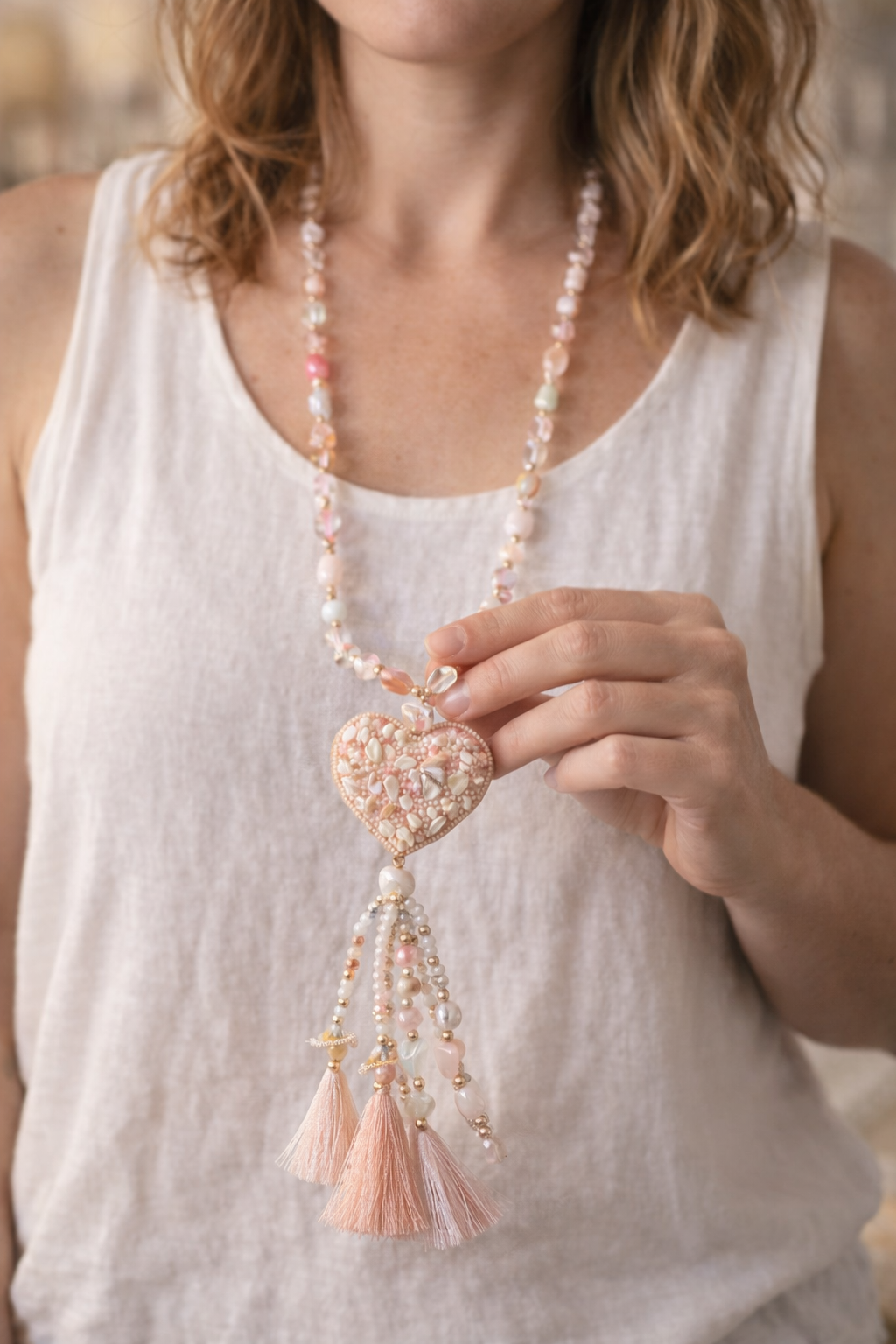 Femme portant un sautoir bohème long avec pendentif cœur et pompons