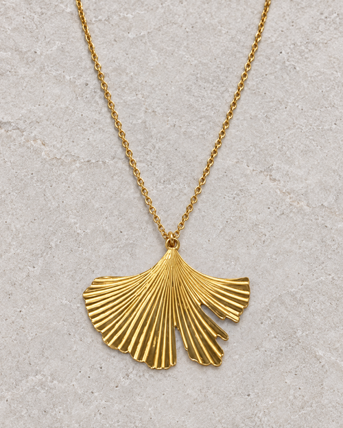 Vue retouchée du pendentif feuille de ginkgo doré et de ses nervures sur pierre claire.
