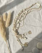 Sautoir multi-rangs perles bois naturel et nacre, breloques fleur et cœur dorées, vue flatlay ambiance bohème