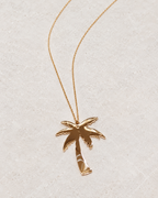Photo retouchée du pendentif palmier doré Palm Tree et de sa chaîne sur pierre claire.
