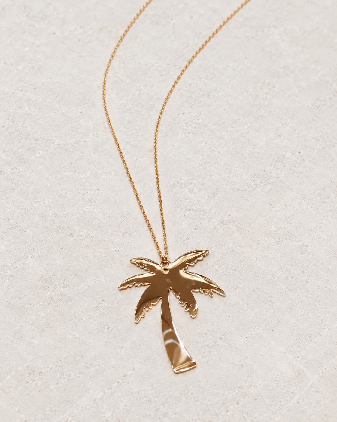 Photo retouchée du pendentif palmier doré Palm Tree et de sa chaîne sur pierre claire.