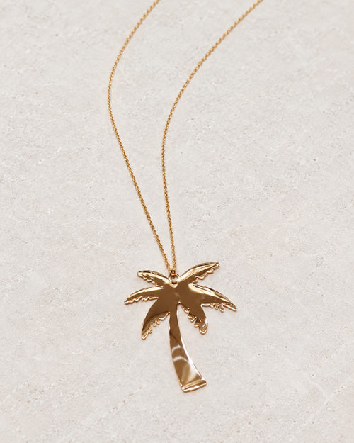 Photo retouchée du pendentif palmier doré Palm Tree et de sa chaîne sur pierre claire.