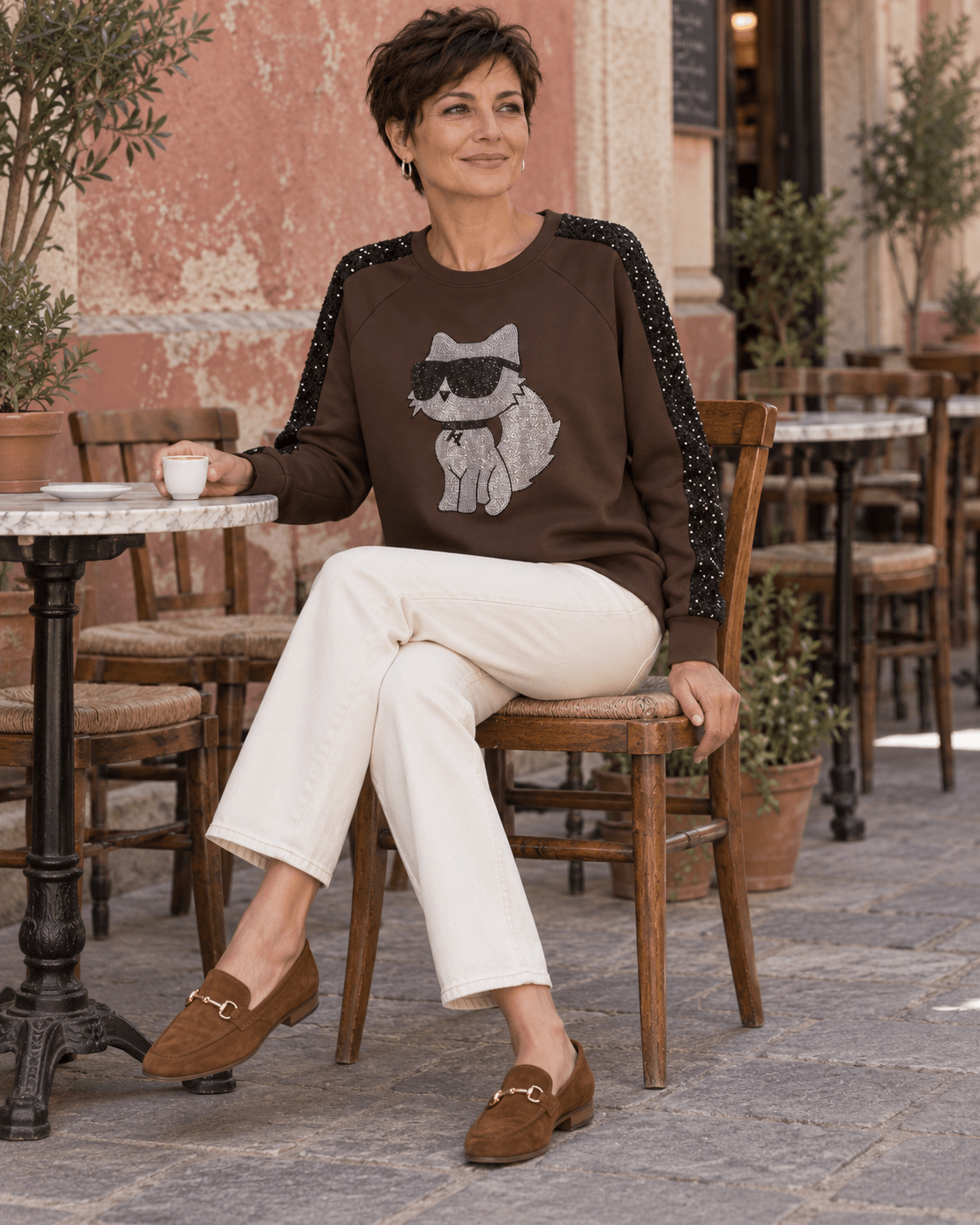 Femme assise en terrasse avec le sweat Catty Chic chocolat et un jean écru