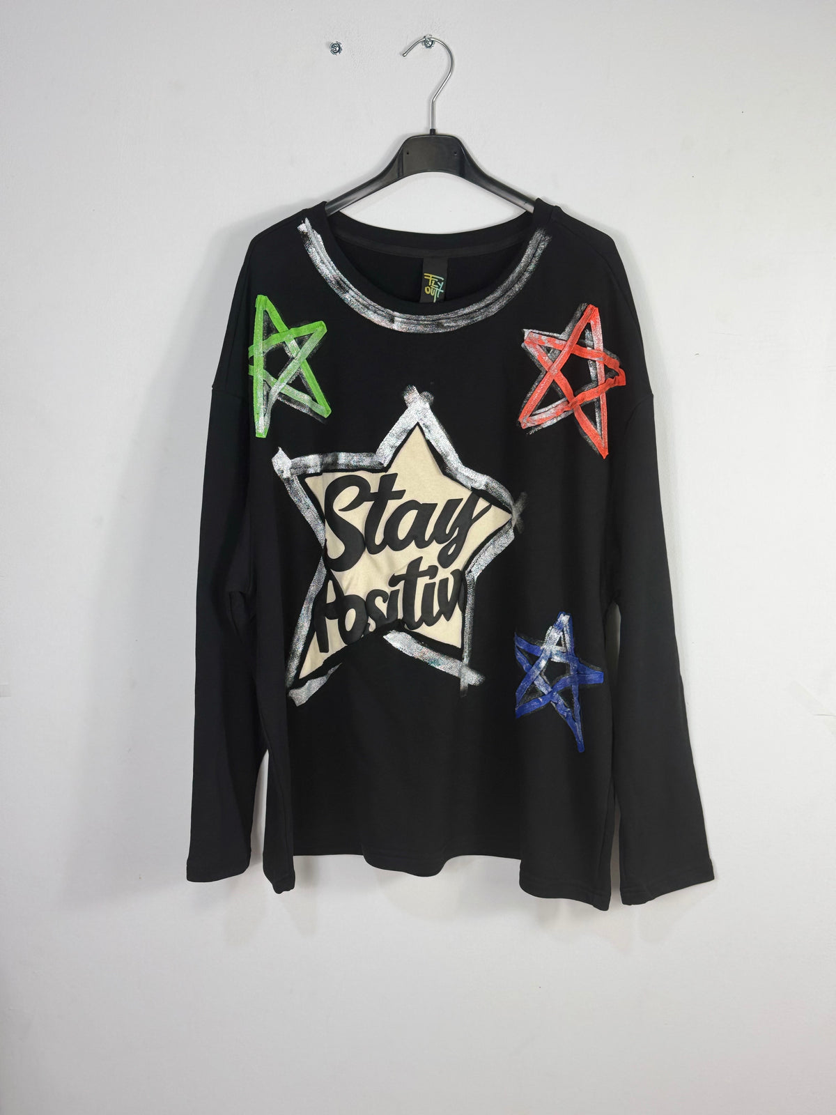 Sweat Eva noir porté de face, grande étoile Stay Positive et étoiles vertes, corail et bleues. 