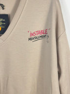 Détail du petit motif Instable mentalement framboise et noir sur le sweat beige.
