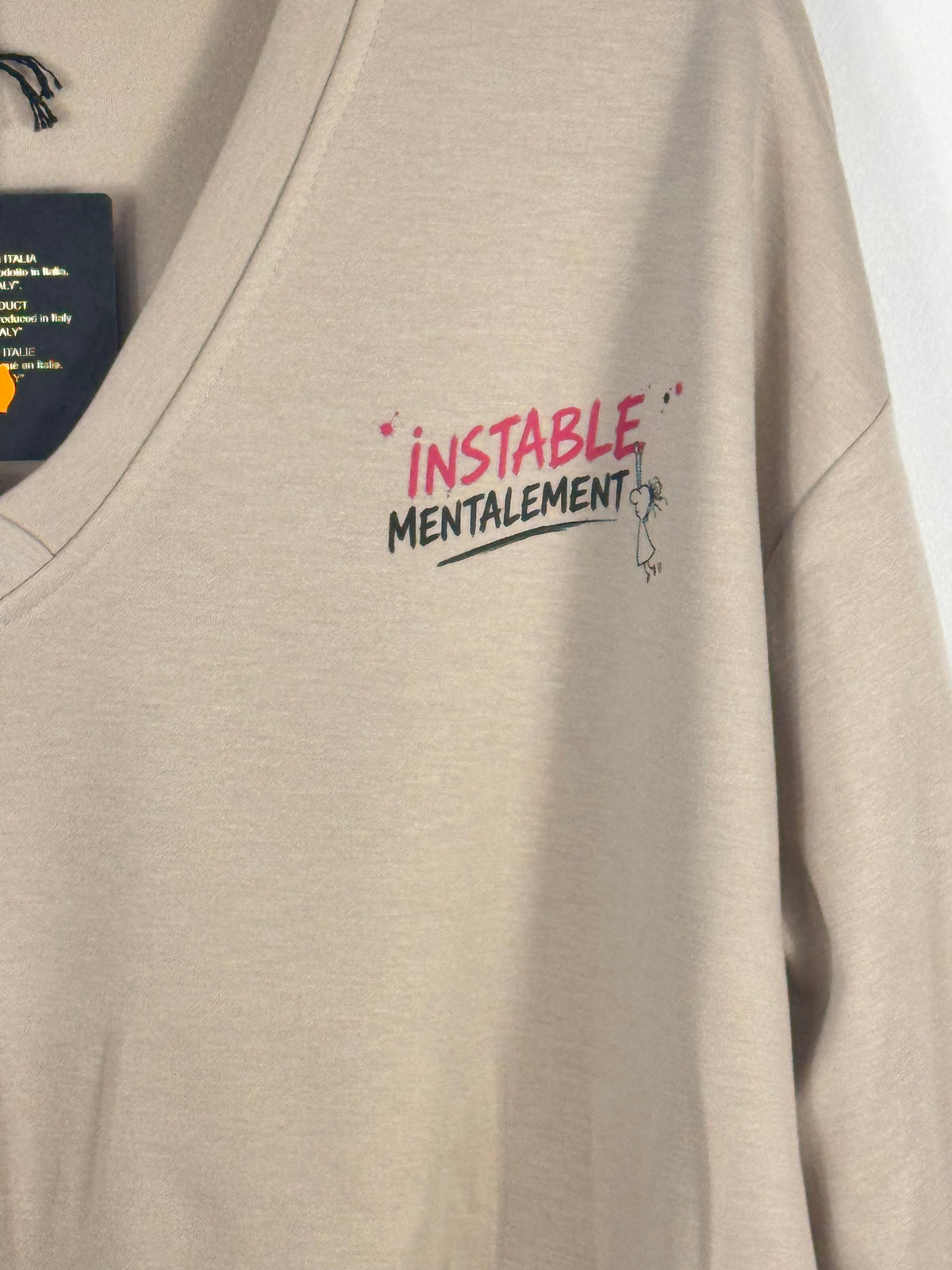 Détail du petit motif Instable mentalement framboise et noir sur le sweat beige.