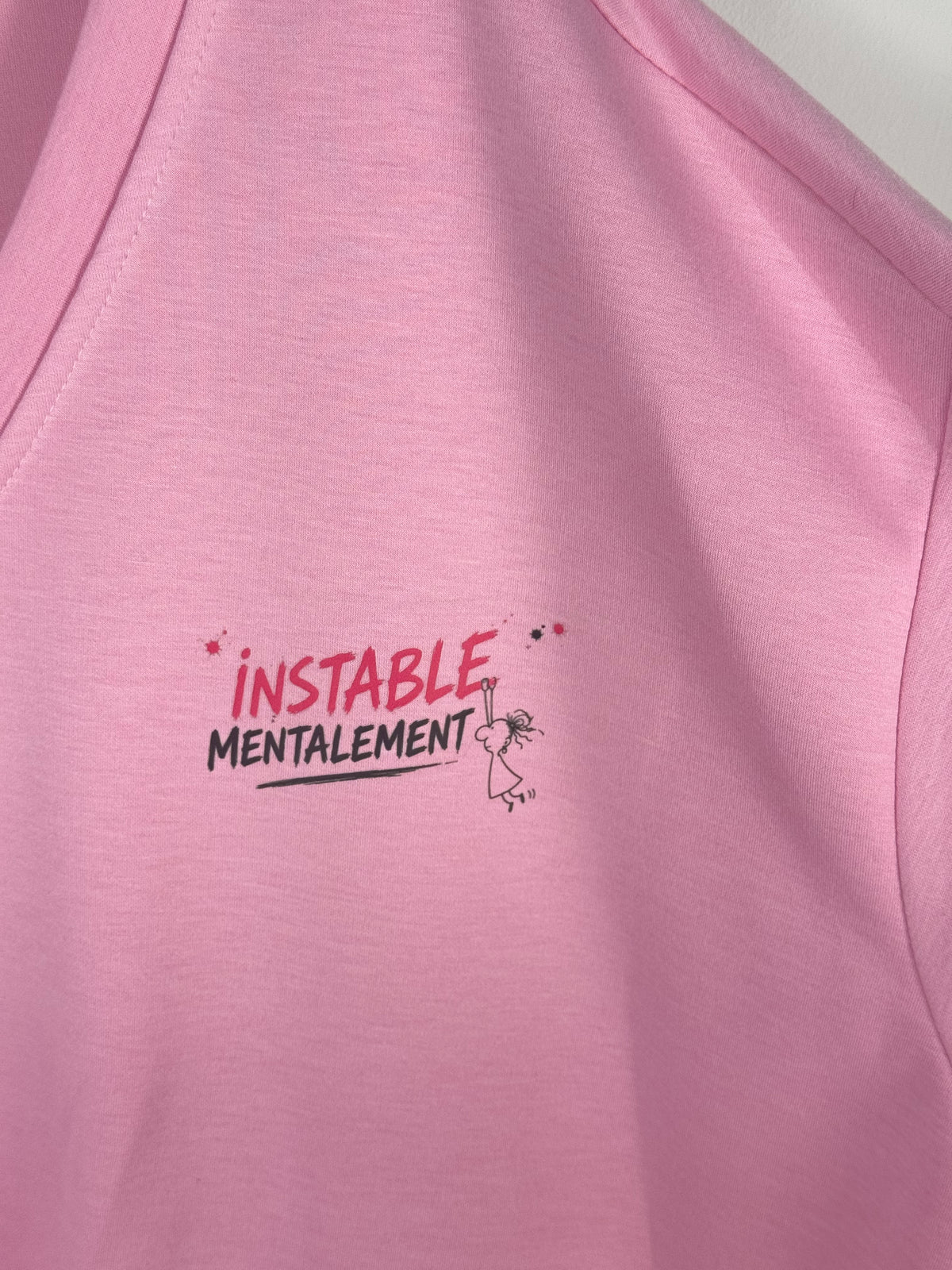 Gros plan du message Instable mentalement et du petit personnage sur le sweat rose.