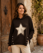 Femme portant le Sweat Luce chocolat à capuche avec grande étoile dorée, strass et boutons bijoux sur les côtés, dans une ambiance italienne