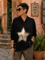 Femme portant le Sweat Luce noir à capuche avec grande étoile dorée, strass et boutons bijoux sur les côtés, dans une ruelle italienne