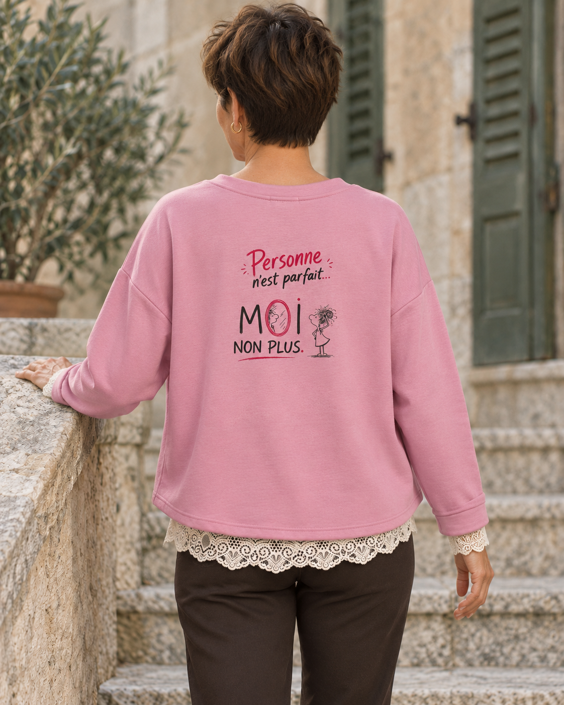 Dos du sweat rose porté, avec le grand motif Personne n’est parfait… MOI NON PLUS et la dentelle écrue dépassant dans le bas.