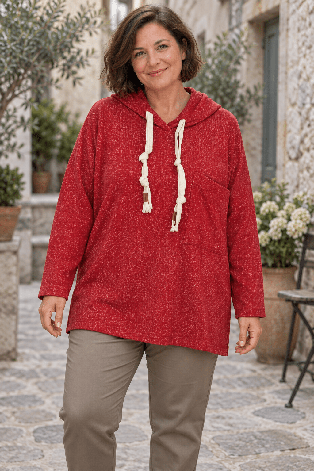 Sweat rouge chiné à capuche porté avec un pantalon taupe, cordons écrus et poche décalée visibles.