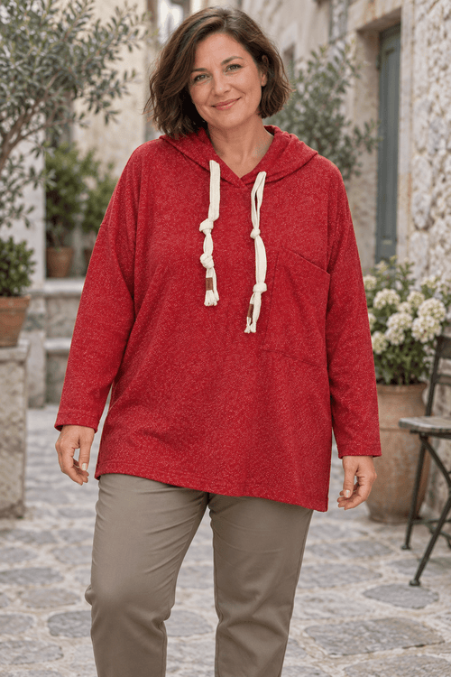 Sweat rouge chiné à capuche porté avec un pantalon taupe, cordons écrus et poche décalée visibles.
