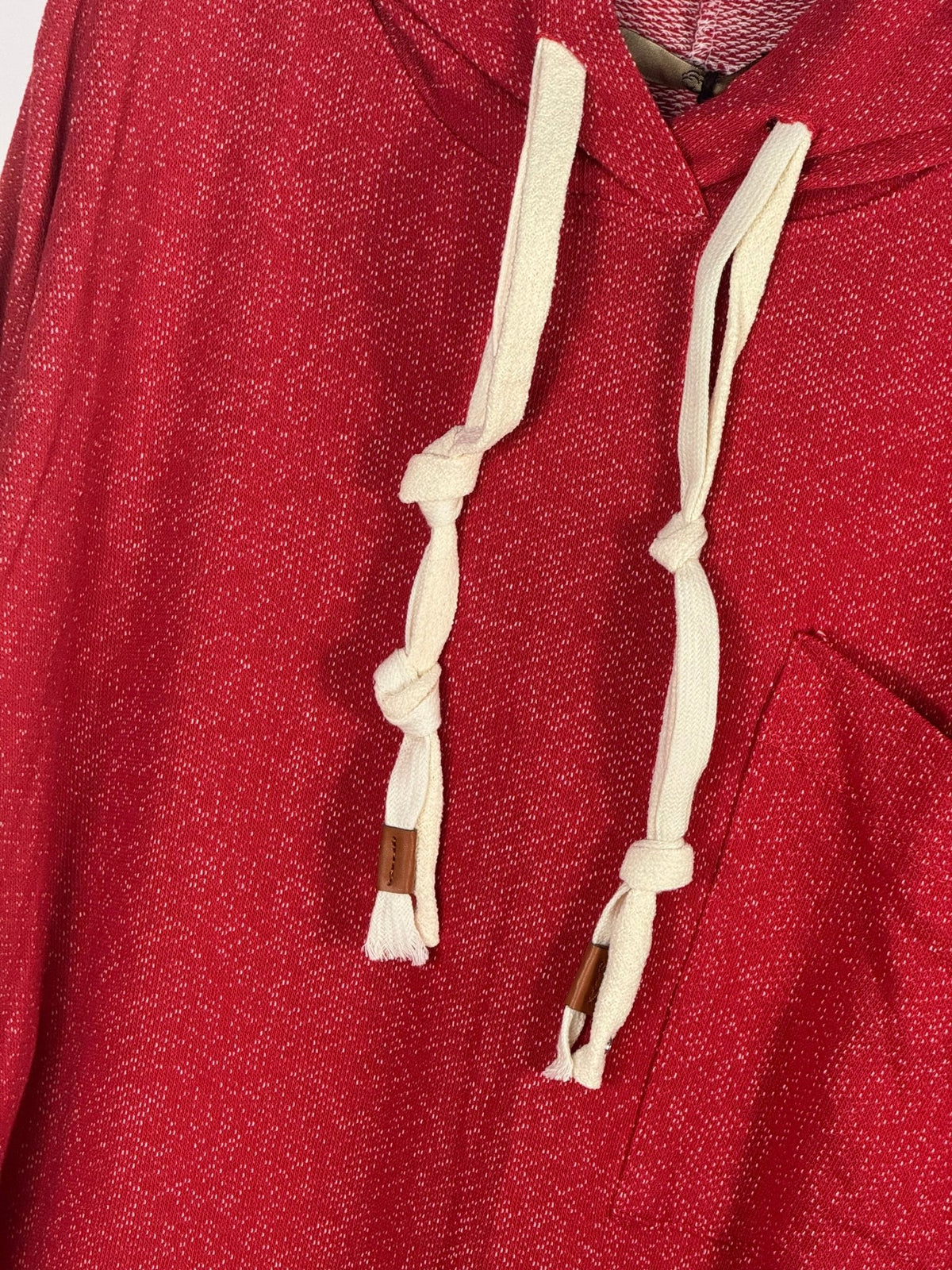 Photo rapprochée des cordons écrus à nœuds et pattes brunes sur le sweat rouge chiné.