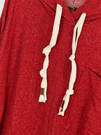Détail du sweat rouge chiné, cordons écrus noués avec pattes brunes et bord de la poche décalée.