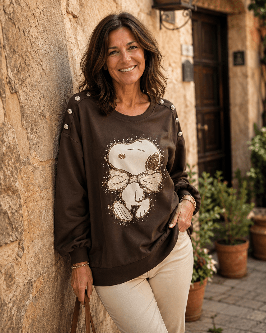 Femme portant le sweat Snoopy chocolat à strass avec pantalon écru dans une ruelle italienne