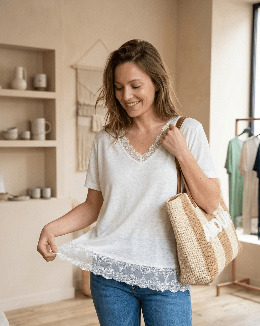 Femme portant un top blanc en viscose avec col V et bordure en dentelle, tenant un sac cabas en paille marqué Amour.