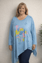 Tunique asymétrique oversize bleu ciel imprimé Los Angeles 1978 multicolore et découpes étoiles, manches longues, ourlet mouchoir, portée avec jean marine