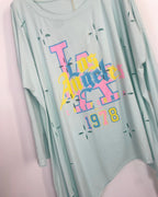 Gros plan sur l'imprimé Los Angeles California 1978 de la tunique vert d'eau : typographie gothique rose, jaune et bleu sur jersey vert menthe à découpes étoiles