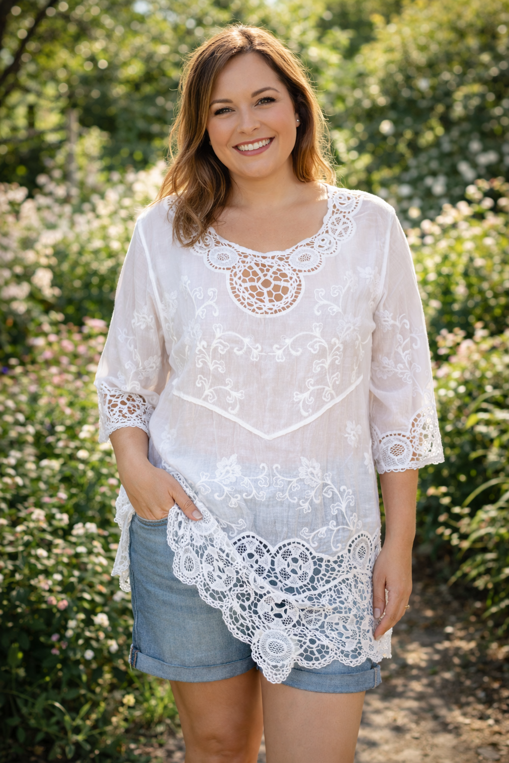 Tunique blanche bohème avec dentelle crochet et broderies florales portée par femme en jardin ensoleillé