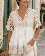 Femme naturelle de 50 ans portant une tunique beige bohème fluide avec dentelle et bijoux discrets, look estival chic dans une ambiance méditerranéenne.