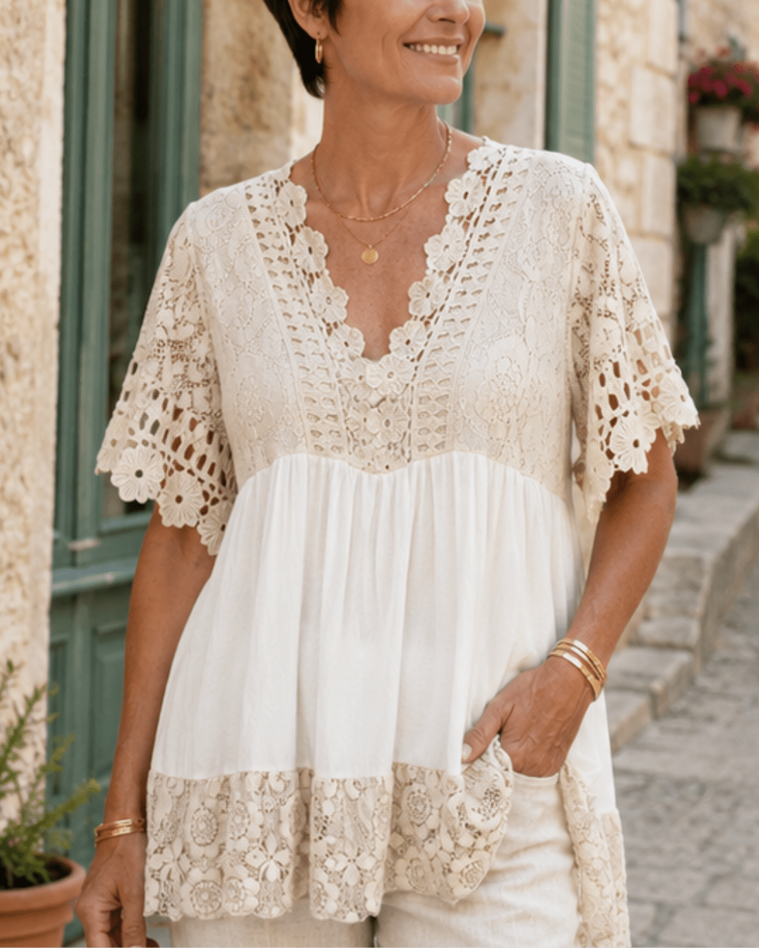 Femme naturelle de 50 ans portant une tunique beige bohème fluide avec dentelle et bijoux discrets, look estival chic dans une ambiance méditerranéenne.