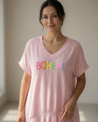 Femme de 45 à 50 ans portant une tunique bohème rose BOHEME avec pantalon blanc, bijoux discrets