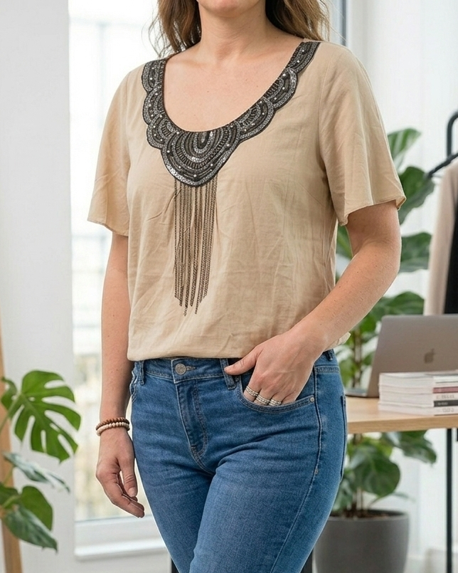 Blouse beige avec broderies de papillons et fleurs, portée avec un jean bleu.