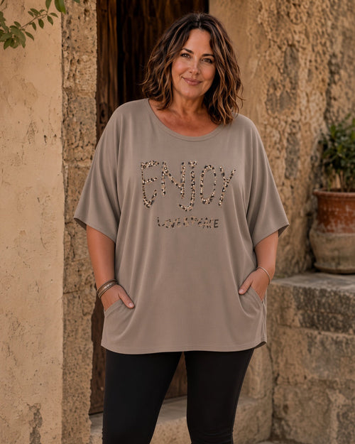 Femme grande taille portant la tunique Gioia taupe à motif Enjoy léopard et strass dans une ambiance italienne