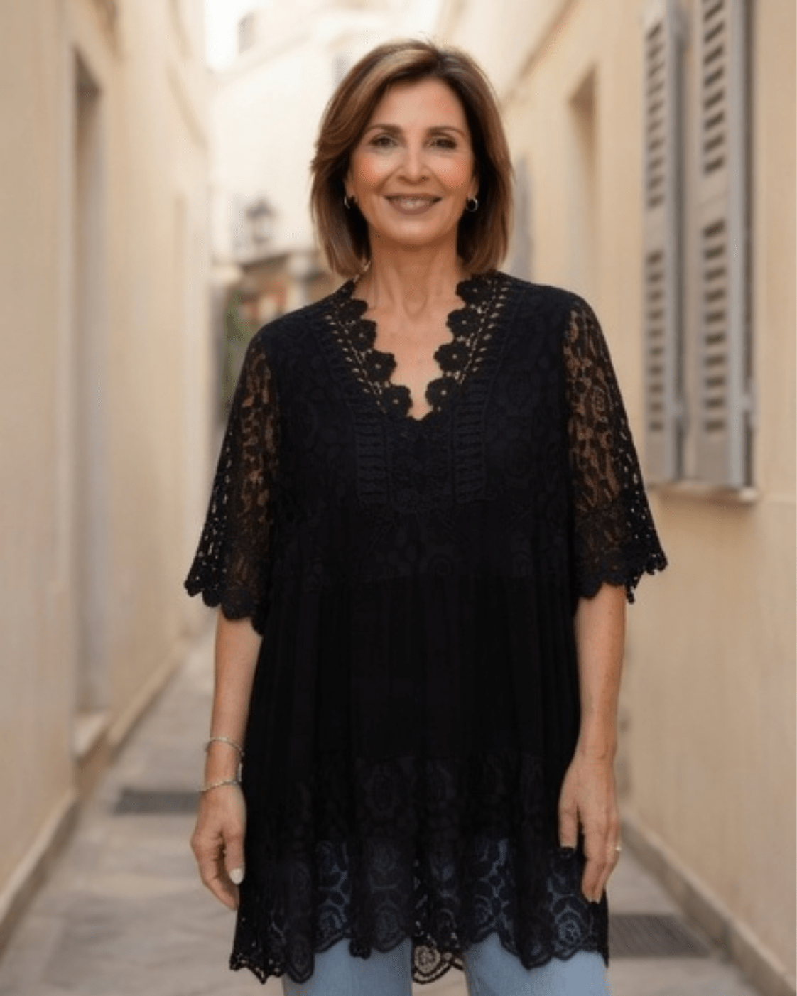 Femme naturelle de 50 ans portant une tunique noire bohème fluide avec dentelle et bijoux discrets, look estival chic dans une ambiance méditerranéenne.