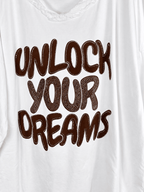 Photo retouchée du message brun Unlock Your Dreams et de ses strass sur la tunique blanche.